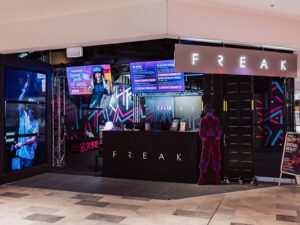 Photo of FREAK Surfers Paradise venue. Silver sign that says FREAK. TV Screens showing people playing virtual reality.