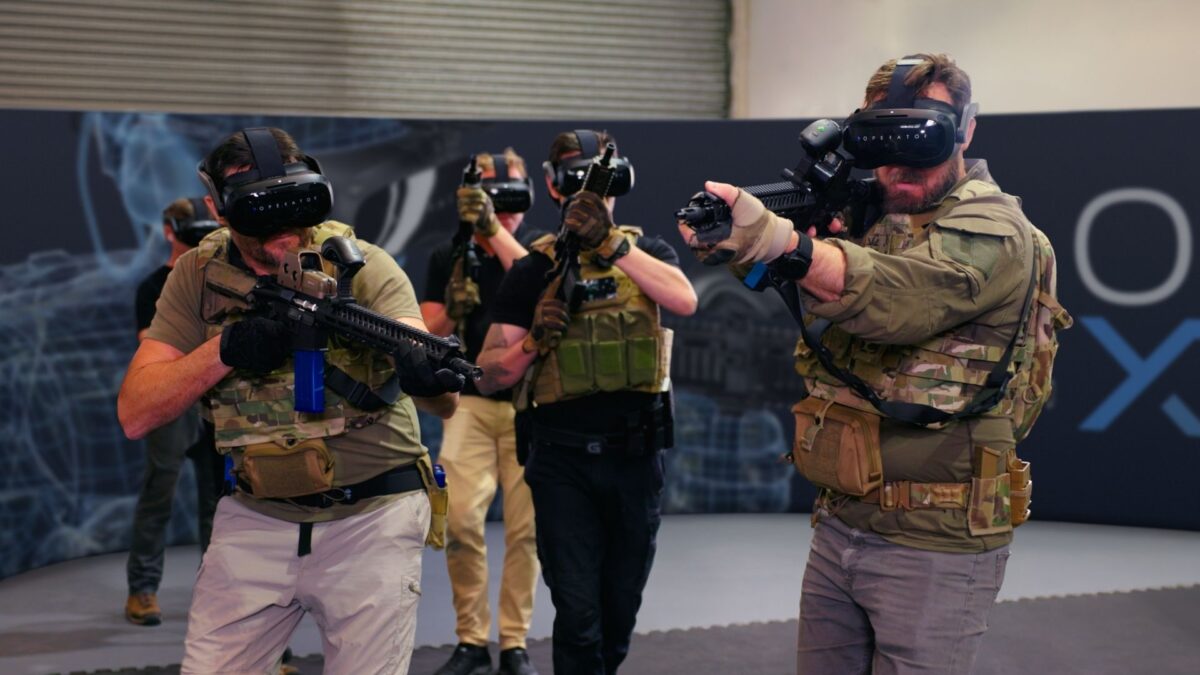 5 military personnel wearing army cams and VR headsets, completing a virtual reality training scenario with their rifles drawn.